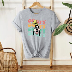 May include: A gray t-shirt with a colorful retro graphic of Goofy's face and the word "Goofy" repeated in a stacked design.