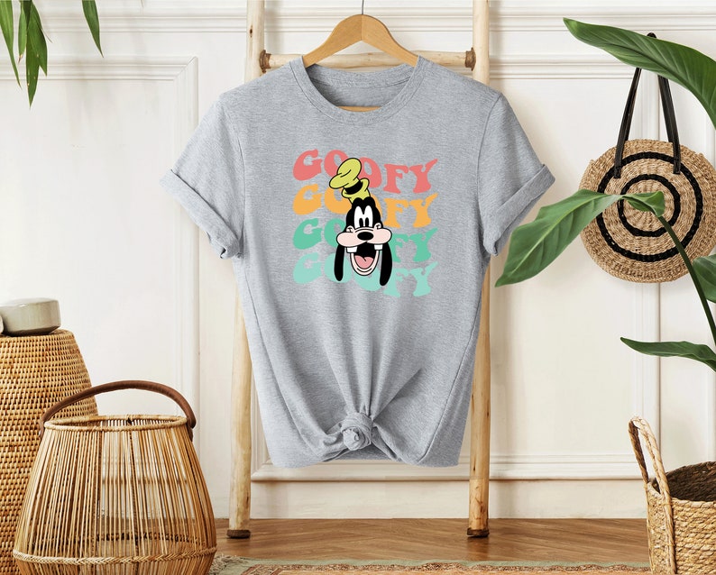 May include: A gray t-shirt with a colorful retro graphic of Goofy's face and the word "Goofy" repeated in a stacked design.
