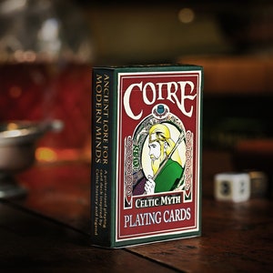 Peut inclure: Un jeu de cartes "Coire Celtic Myth Playing Cards" avec un design rouge et vert. La boîte présente une illustration d'un personnage celtique et le texte "Ancient Lore for Modern Minds". Le jeu est de taille poker et inspiré de l'histoire et de la légende celtiques.