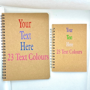 May include: Two brown spiral notebooks with the text "Your Text Here" and "23 Text Colours" on the front covers. The notebooks are on a white surface.