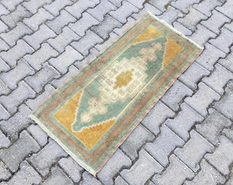 May include: A rectangular area rug featuring a central geometric medallion in shades of cream, mustard yellow, and sage green. The rug is framed by a brown border and finished with short, light-colored fringe along the two shorter ends.
