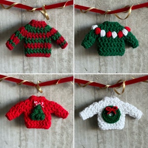 May include: Four crocheted Christmas decorations shaped like jumpers, each with a different design. The jumpers are red and green with white accents. The decorations are hanging from a red ribbon.