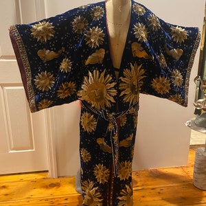 May include: A long, dark blue velvet robe with a gold embroidered sun pattern. The robe has a tie belt and is decorated with gold beads.
