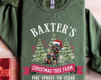 May include: Green sweatshirt with the text "BAXTER'S" above a dog wearing a Santa hat and Christmas lights. Below the dog is a banner that reads "CHRISTMAS TREE FARM" and the words "PINE • SPRUCE • FIR • CEDAR".