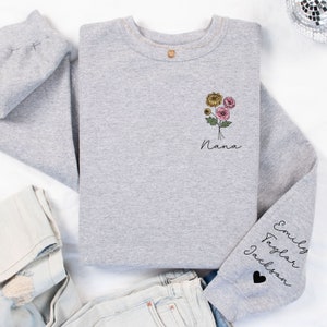 May include: Gray sweatshirt with a floral design and the word "Nana" on the front. The sleeve has the names "Emily Taylor Jackson" and a black heart.