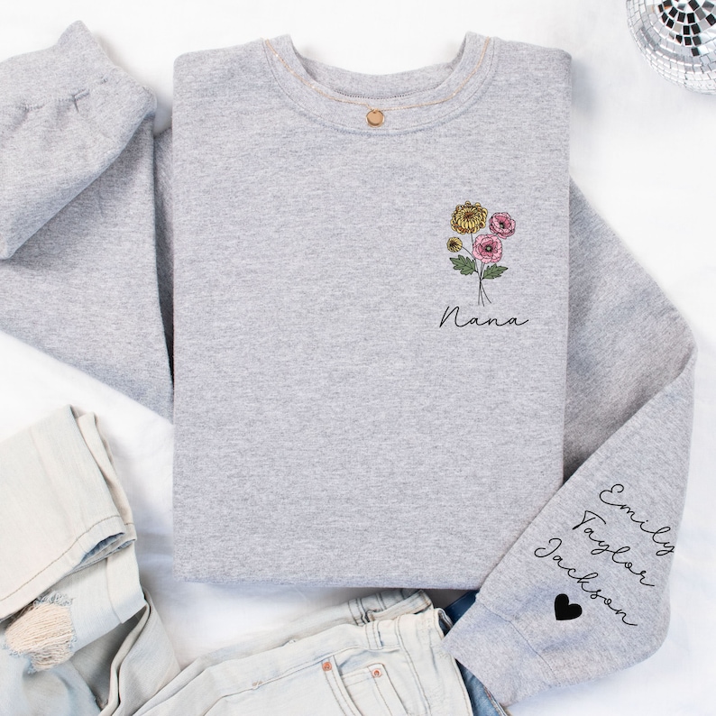May include: Gray sweatshirt with a floral design and the word "Nana" on the front. The sleeve has the names "Emily Taylor Jackson" and a black heart.