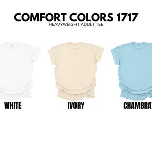 May include: Three t-shirts in different colors: white, ivory, and Chambray. The t-shirts are all the same style, with a crew neck and short sleeves. The text "COMFORT COLORS 1717 HEAVYWEIGHT ADULT TEE" is displayed above the t-shirts.