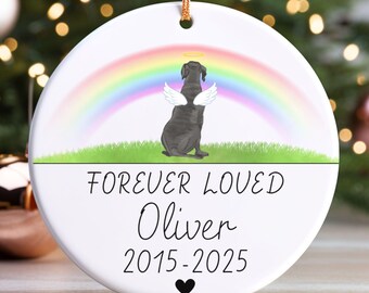 May include: A round white ceramic ornament featuring a black dog with white angel wings and a halo, sitting on green grass under a rainbow. The text reads FOREVER LOVED, Oliver, and 2015-2025, with a small black heart at the bottom.