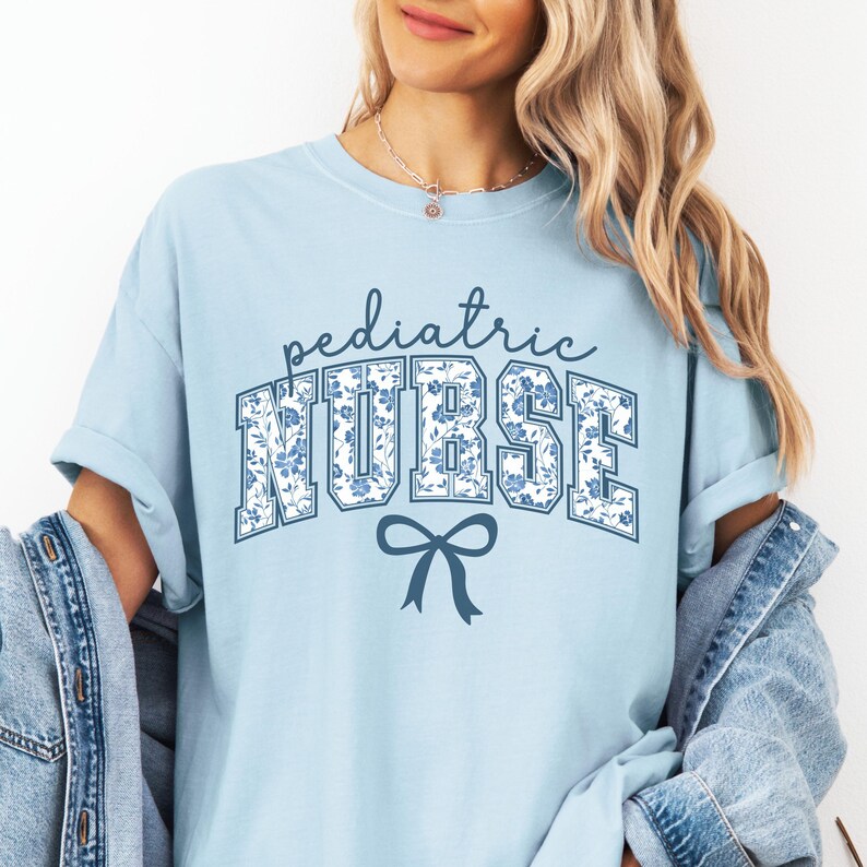 May include: Light blue t-shirt with a floral print design that says "pediatric NURSE" in blue letters with a blue bow underneath.