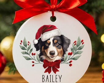 May include: A round white Christmas ornament featuring a dog wearing a Santa hat. The dog has black, brown, and white fur, with the name "BAILEY" and the year "2025" printed below. A red bow and ribbon complete the festive design.