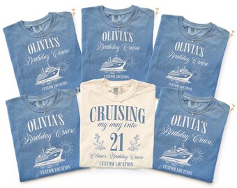 May include: Five blue t-shirts and one cream t-shirt featuring white and blue graphic prints. The blue shirts display a cruise ship, sun, and the text "OLIVIA'S Birthday Cruise CUSTOM LOCATION". The cream shirt features "CRUISING my way into 21".