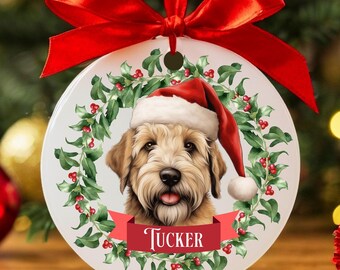 May include: A round Christmas ornament featuring a dog wearing a Santa hat, surrounded by a holly wreath. The dog's name, "Tucker," is displayed on a red banner. A red ribbon is attached for hanging.
