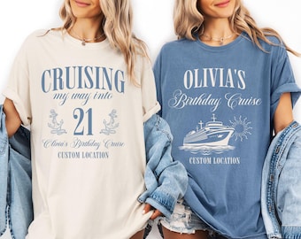 May include: Two t-shirts, one cream and one blue, with cruise-themed designs. The cream shirt says "Cruising my way into 21" with anchors and "Olivia's Birthday Cruise." The blue shirt says "Olivia's Birthday Cruise" with a cruise ship.