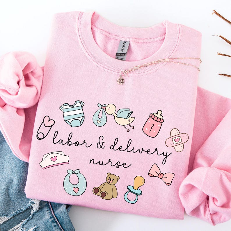 May include: Pink sweatshirt with a cute design featuring baby-related icons and the text "labor & delivery nurse".