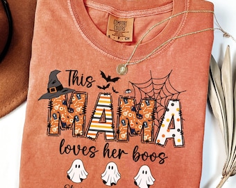 May include: Orange Comfort Colors t-shirt with a Halloween-themed design. The shirt features the text "This MAMA loves her boos" with a witch hat, bats, and spiderwebs. Below are three ghost illustrations and names.