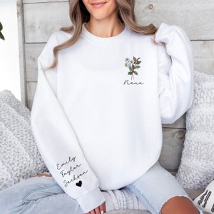 May include: White sweatshirt with a floral design and the word "Nana" on the front. The sleeve has the names "Emily", "Taylor", and "Jackson" with a heart.