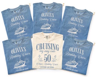 May include: A collection of blue and cream-colored t-shirts with cruise-themed graphics. The blue shirts feature the text "OLIVIA'S Birthday Cruise" and a ship illustration. The cream shirt says "Cruising my way into 50".