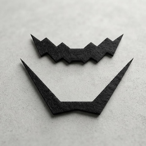 Puede incluir: Dos recortes de fieltro negro con forma de boca dentada y una pieza de barbilla puntiaguda. La pieza superior presenta una serie de dientes triangulares afilados, mientras que la pieza inferior es una forma angular ancha con dos extremos largos.
