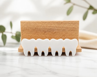 May include: A rectangular light brown wooden block stand featuring a row of four white, flat, tooth-shaped cutouts attached to the front. The wooden stand has a horizontal slot along the top edge, and the tooth shapes are arranged side by side.