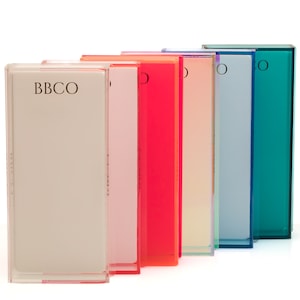 May include: A set of six clear acrylic boxes with different colored bases. The boxes are arranged in a row from left to right, with the colors progressing from light pink to teal. The box on the left has the text "BBCO" printed on the front.