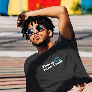 May include: A person wearing a black t-shirt with the text "This is how I roll." and a dice graphic. They are wearing brown pants and white sneakers with colorful accents.