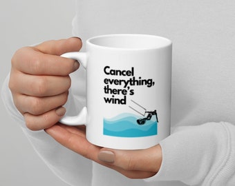 May include: White ceramic mug with a blue and black graphic of a person waterskiing. The text on the mug reads "Cancel everything, there's wind."