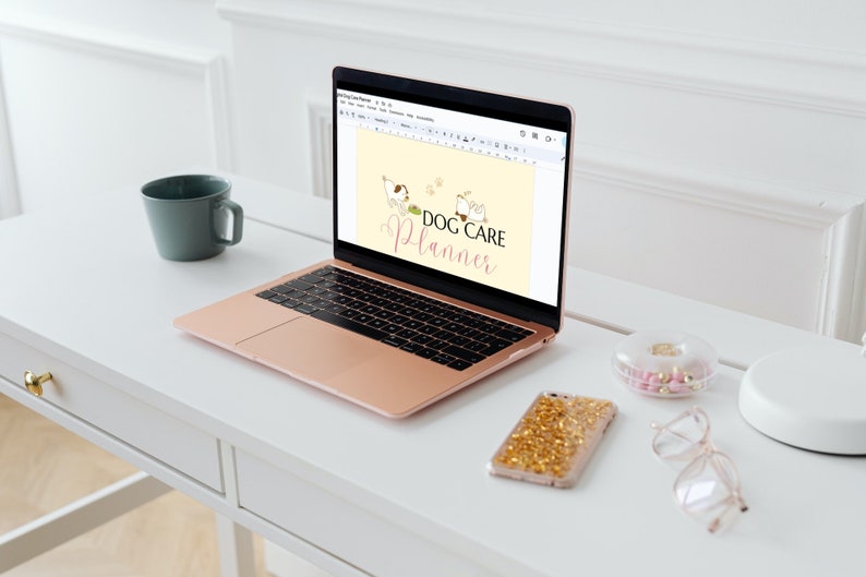 May include: A rose gold laptop computer open to a Google Docs document with the text "DOG CARE PLANNER" in pink and white lettering. The document has a cartoon image of two dogs. The laptop is on a white desk with a white mug, a clear container with pink and gold pills, a gold glitter phone case, and clear glasses.