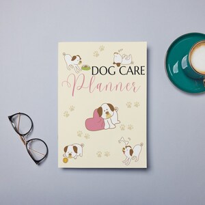 May include: A cream-colored planner with the text "DOG CARE Planner" in pink and brown lettering. The cover features illustrations of dogs in various poses, including a dog sleeping, a dog eating from a bowl, a dog playing with a bone, and a dog with a pink heart.