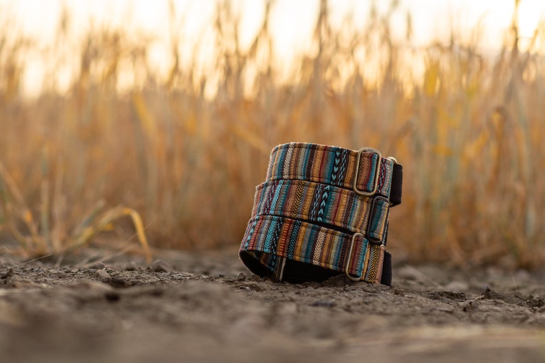 May include: Three colorful dog collars stacked on top of each other. The collars are made of woven fabric with a geometric pattern in shades of blue, orange, yellow, and brown. The collars have silver metal buckles.