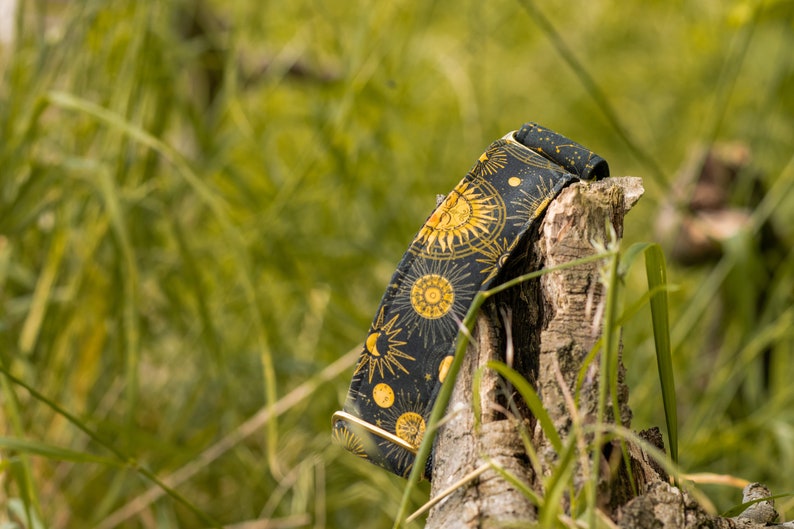 May include: A black and gold dog collar with a celestial pattern featuring suns, moons, and stars.
