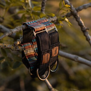 May include: Two dog collars, one black with a brown leather patch and the other with a colorful patterned fabric. Both collars have silver metal D-rings.