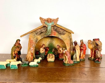 May include: A vintage Nativity scene with a stable, figures of Mary, Joseph, baby Jesus, the Three Wise Men, and animals. The figures are painted in various colors, including gold, red, and green. The stable has a weathered appearance.