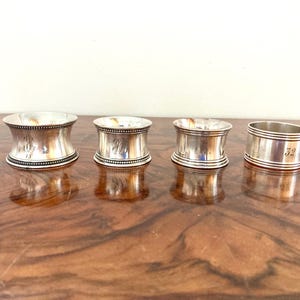 Può includere: Quattro anelli portatovaglioli d'argento con diversi design. Due anelli hanno una forma a clessidra, uno è cilindrico e uno ha una fascia più larga. Ogni anello ha un design inciso o un numero diverso.