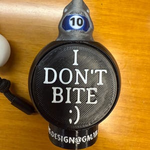 May include: A black and gray shark-themed bottle stopper with the text "I DON'T BITE :) ". The shark's head has a blue and white number 10. The bottom of the stopper has the text "S.DESIGN@GMAIL".
