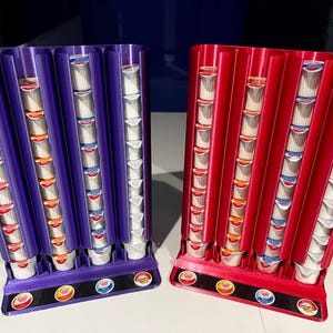 May include: Two coffee pod holders, one purple and one red, each with five columns of pods. The holders are made of plastic and have a sleek, modern design.