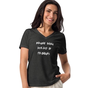 May include: A dark heather grey V-neck t-shirt with the text "Imagine being afraid of pronouns" printed in white.