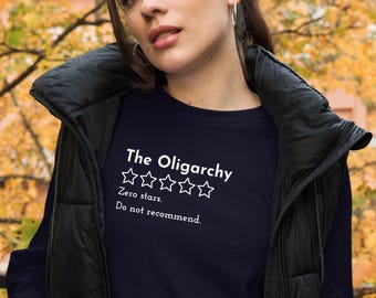 May include: A navy blue long-sleeved shirt with white text that reads "The Oligarchy" with five empty white stars below the text and the words "Zero stars. Do not recommend." below the stars.