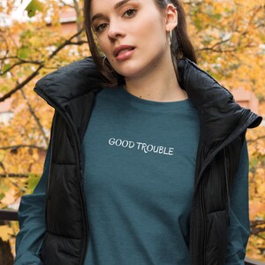 May include: A teal blue long-sleeved shirt with the text "GOOD TROUBLE" in white lettering.