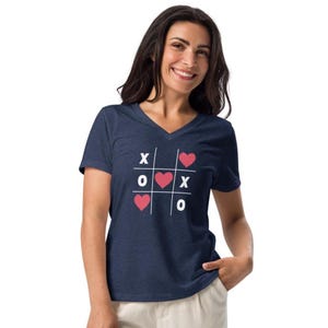 May include: A navy blue V-neck t-shirt with a white tic-tac-toe board design featuring pink hearts. The text "X O X O" is printed on the board.