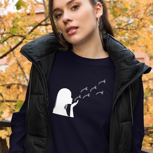 May include: A navy blue long-sleeved sweatshirt with a white silhouette of a person blowing dandelion seeds. The design features a woman blowing on a dandelion, sending seeds flying in the air.