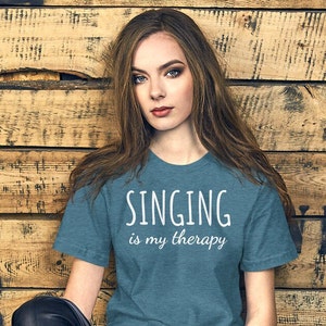 May include: Teal t-shirt with the text "SINGING is my therapy" in white. The shirt is made of a soft material and has short sleeves. The shirt is a casual wear item.