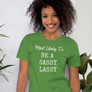 May include: Green t-shirt with white text that reads "Most Likely To Be A Sassy Lass"