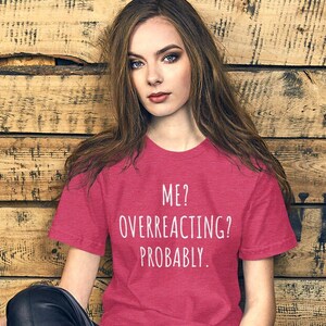 May include: A pink heather t-shirt with white text that reads "ME? OVERREACTING? PROBABLY."