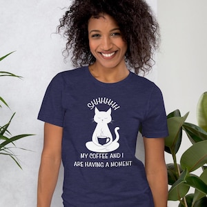 May include: A navy blue t-shirt with a white graphic of a cat meditating with a cup of coffee. The text on the shirt reads "Shhhhhhh My coffee and I are having a moment."