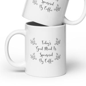 May include: White ceramic coffee mug with black text that reads "Today's Good Mood Is Sponsored By Coffee" and a design of coffee beans around the text.