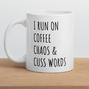 May include: White ceramic coffee mug with black text that reads "I run on coffee chaos & cuss words".