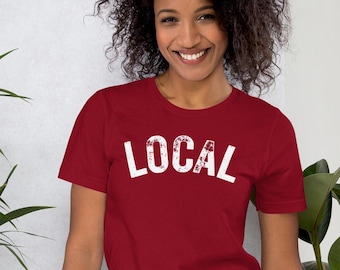 May include: A red short-sleeved t-shirt with the word "LOCAL" printed in white on the front. The text has a distressed, vintage look.
