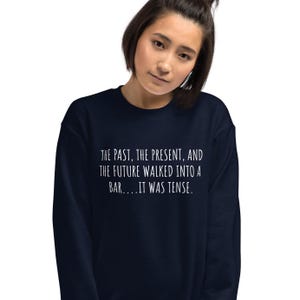 May include: A navy blue sweatshirt with a white graphic print that reads "THE PAST, THE PRESENT, AND THE FUTURE WALKED INTO A BAR....IT WAS TENSE."