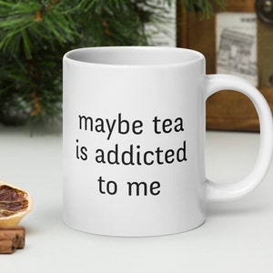 Peut inclure: Une tasse en céramique blanche avec du texte noir qui dit "peut-être que le thé est accro à moi".