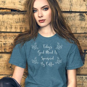 May include: A teal blue t-shirt with a white graphic that reads "Today's Good Mood Is Sponsored By Coffee" with coffee bean illustrations.